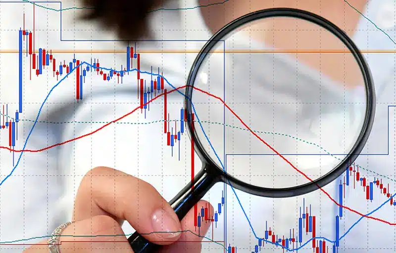 Market Analysis A bar and line graph close up with a woman holding a magnifying glass up to it.