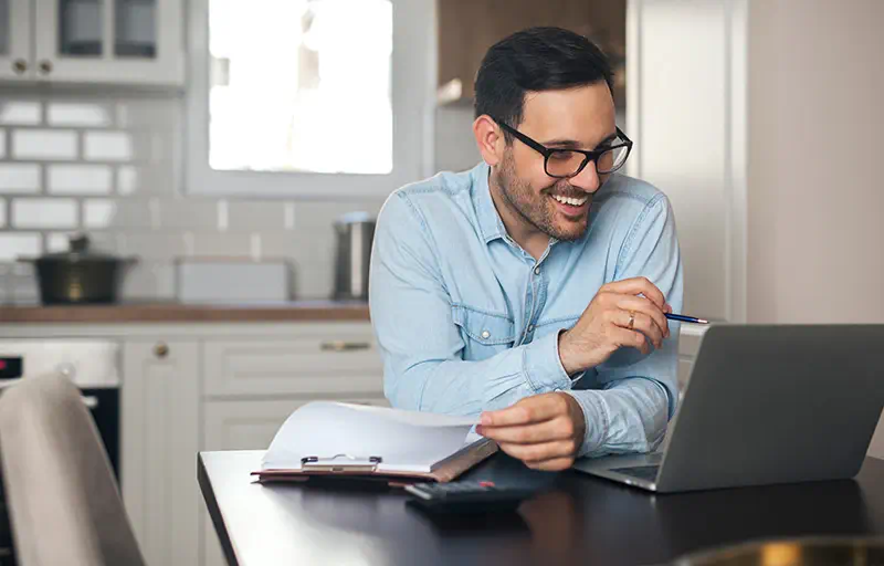 Property Search A business man smiles at his laptop while working at home.