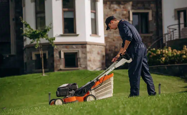 Fuel powered lawn mover, cutting the grass. Professional gardener is on the lawn.