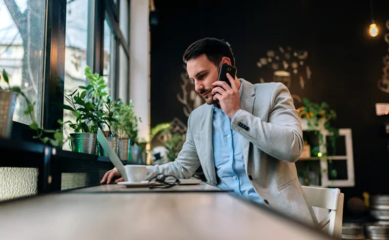 Modern businessman talking on a smartphone while working on laptop in the cafe.