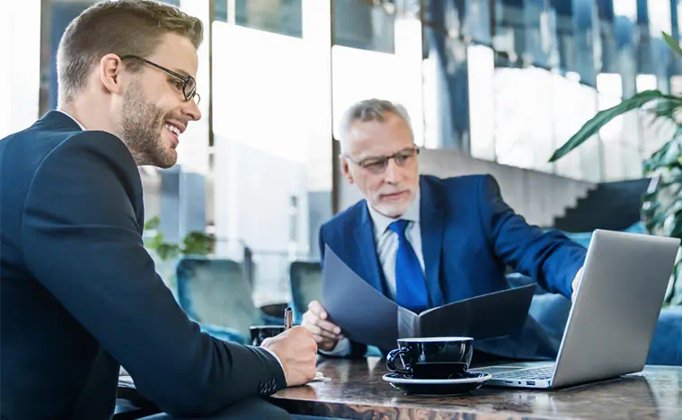 Two businessmen employees planning sales, research or financial strategy in company using laptop in lobby of modern office. Teamwork meeting, gadget and business people in workplace.