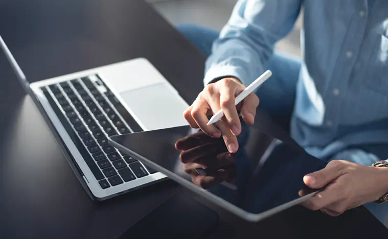 Young casual business woman sitting on the floor using stylus pen and digital tablet, working on laptop computer