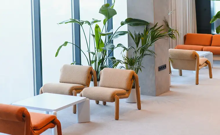 Contemporary lounge interior showcasing minimalist design with beige and orange seating, a white coffee table, and large potted plants