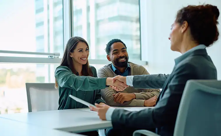 A business woman shakes the hand of a client in a meeting room.